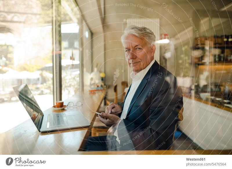 Porträt eines älteren Geschäftsmannes mit Handy und Laptop in einem Café geschäftlich Geschäftsleben Geschäftswelt Geschäftsperson Geschäftspersonen