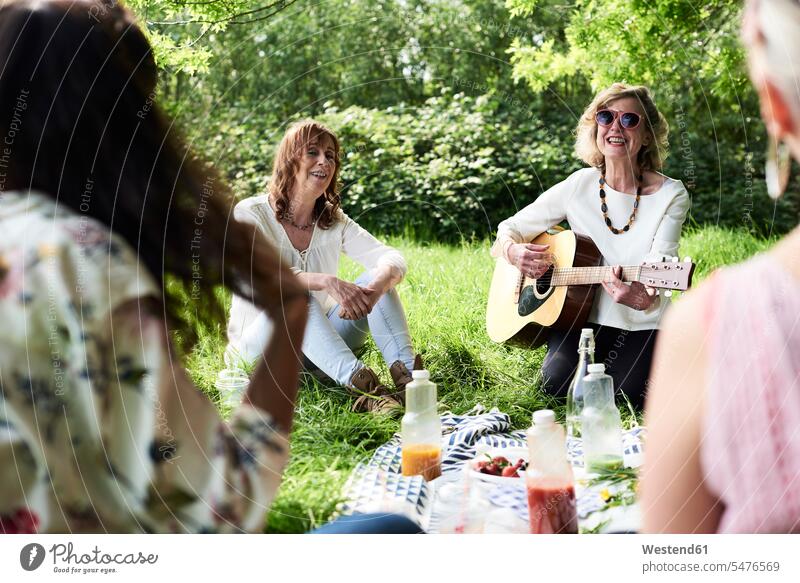 Gruppe von Frauen mit Gitarre haben Spaß bei einem Picknick im Park Parkanlagen Parks Freundinnen Gitarren Spass Späße spassig Spässe spaßig picknicken weiblich