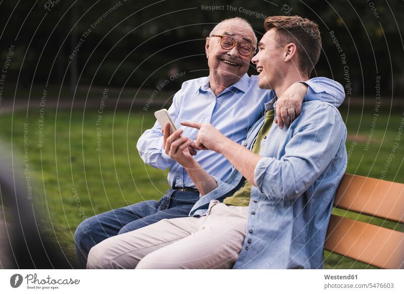 Älterer Mann und Enkel mit Smartphone sitzen zusammen auf einer Parkbank und amüsieren sich Generation Bänke Sitzbank Sitzbänke Parkbänke Handies Handys