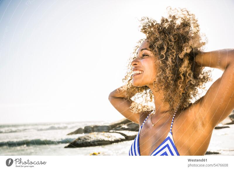 Porträt einer glücklichen jungen Frau am Strand Leute Menschen People Person Personen gelockt gelockte Haare gelocktes Haar lockig lockiges Haar Badebekleidung