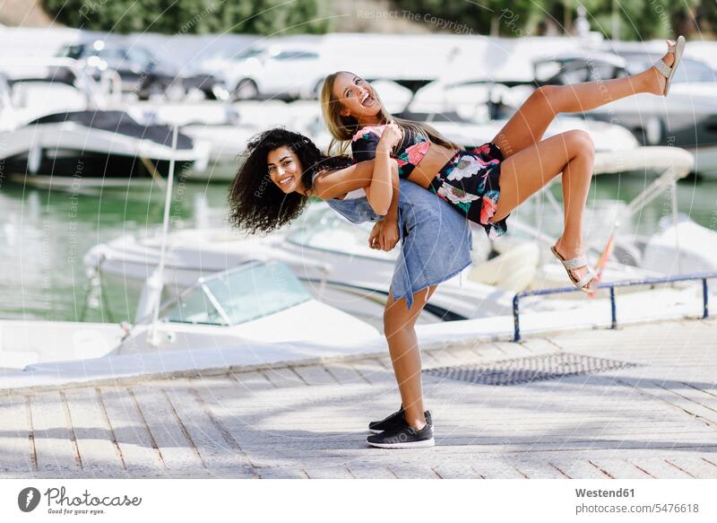 Zwei verspielte junge Frauen an der Uferpromenade im Sommer spielerisch Promenade Promenaden Freundinnen weiblich Sommerzeit sommerlich lachen Freunde