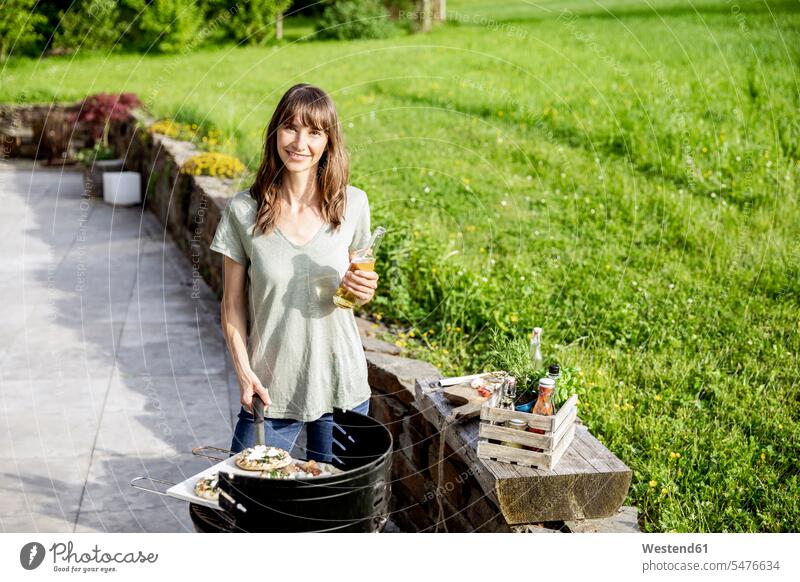 Porträt einer lächelnden Frau, die Essen auf einem Grill zubereitet Leute Menschen People Person Personen Europäisch Kaukasier kaukasisch 1 Ein ein Mensch