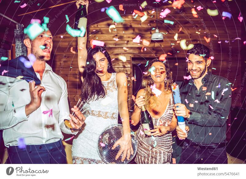 Männliche und weibliche Freunde mit Champagner und Discokugel tanzen inmitten von Konfetti auf einer Party Farbaufnahme Farbe Farbfoto Farbphoto Innenaufnahme