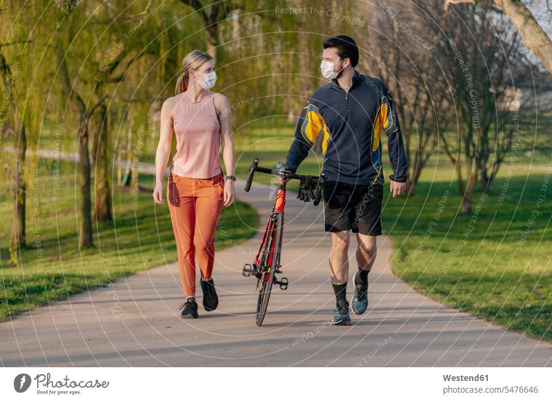 Junges Paar geht während der Coronavirus-Pandemie mit dem Fahrrad auf einem Fußweg im Park spazieren Farbaufnahme Farbe Farbfoto Farbphoto Außenaufnahme außen