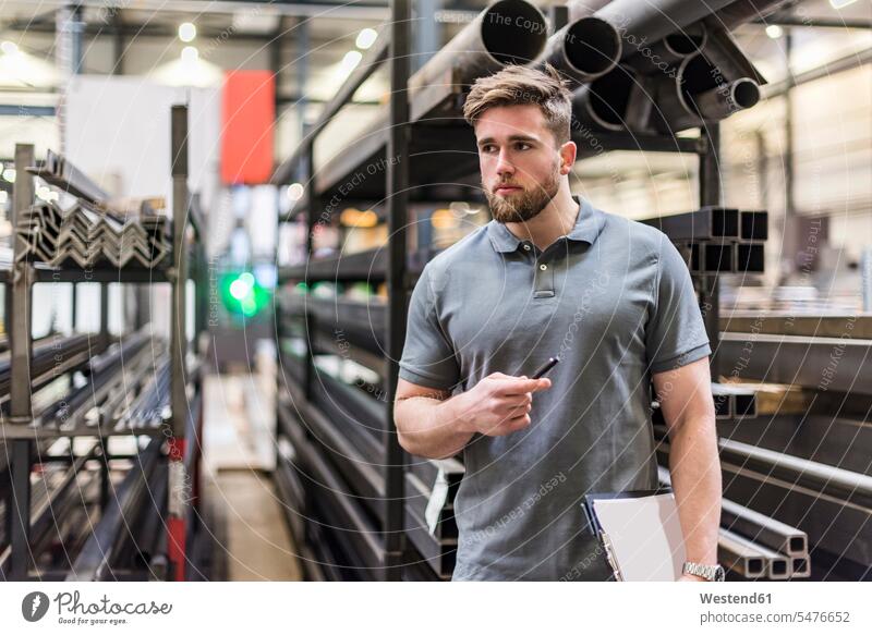 Mann mit Zwischenablage in der Fabrikhalle schaut sich um Fabriken Männer männlich umherblicken umschauen umsehen Klemmbrett Klemmbretter Produktionshalle