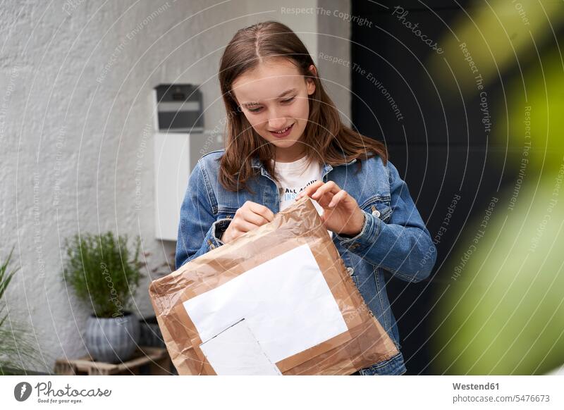 Mädchen steht vor dem Haus und freut sich über ein Paket Briefkästen Pakete Päckchen Nachricht Nachrichten außen draußen im Freien am Tag Tagesaufnahme