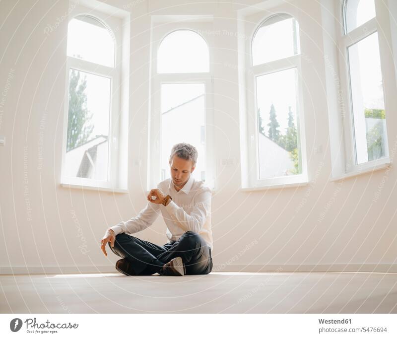 Geschäftsmann sitzt auf dem Boden seines neu renovierten Hauses und überprüft die Zeit Neues Zuhause sitzen sitzend warten auf dem Boden sitzen