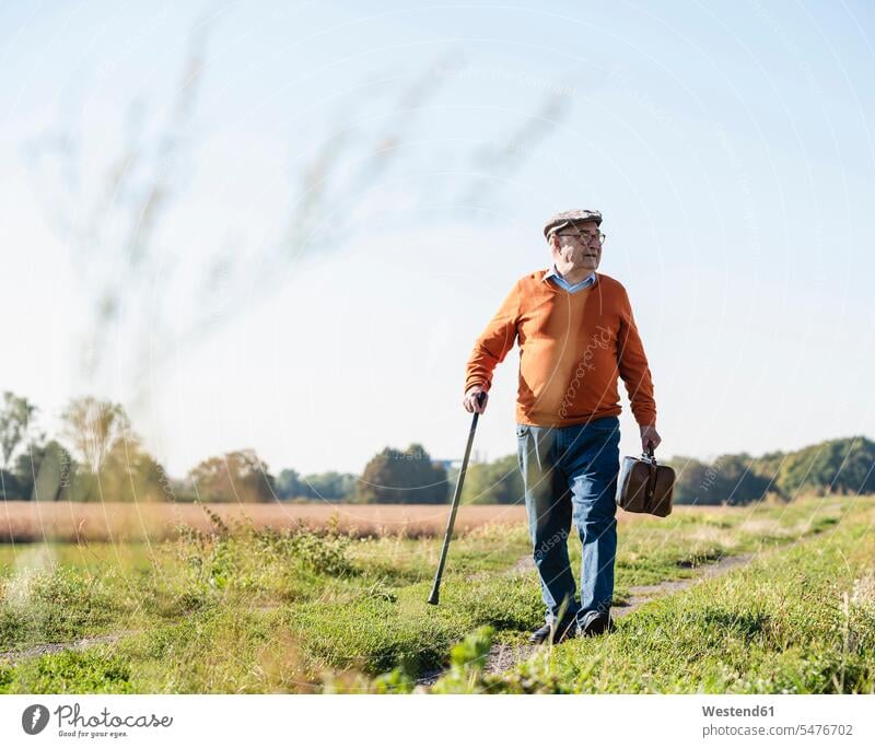 Älterer Mann mit Reisetasche, der in den Feldern spazieren geht tragen transportieren weggehen verlassen weg gehen Reisetaschen gehend Senior ältere Männer
