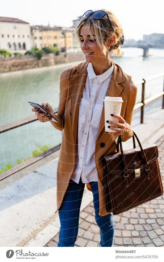 Lächelnde Frau mit Kaffee zum Mitnehmen mit Smartphone in der Stadt Leute Menschen People Person Personen Europäisch Kaukasier kaukasisch 1 Ein ein Mensch eine