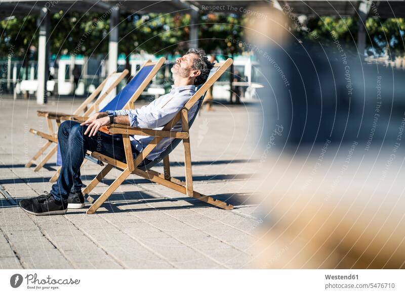 Älterer Mann entspannt im Liegestuhl auf einem Platz in der Stadt staedtisch städtisch sitzen sitzend sitzt Männer männlich Liegestühle Plätze Plaetze