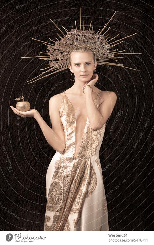 Junge Frau in Kleid mit tiefem Ausschnitt und Kopfbedeckung, hält einen Apfel Modell Modelle Models Kleider Abendkleider golden stehend steht Stil stylisch