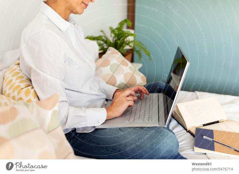 Reife Frau sitzt zu Hause am Bett und benutzt einen Laptop Leute Menschen People Person Personen Alleinstehende Alleinstehender Singles Unverheiratete