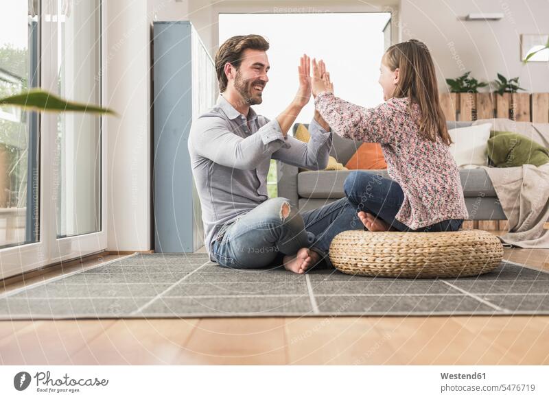 Junger Mann und kleines Mädchen sitzen zu Hause, geben High Five optimistisch Optimismus abklatschen auf dem Boden sitzen auf dem Boden sitzend