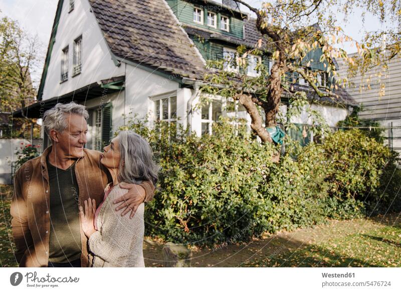 Älteres Ehepaar im Herbst im Garten ihres Hauses entspannen relaxen Arm umlegen Umarmung Umarmungen Jahreszeiten entspanntheit relaxt freuen geniessen Genuss