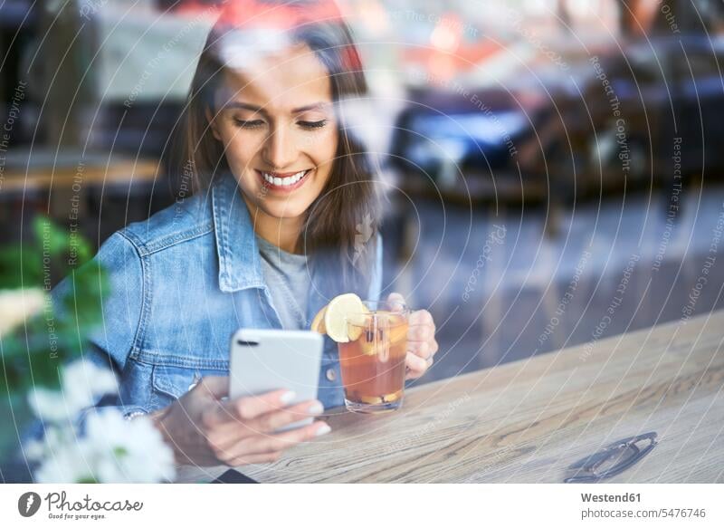 Lächelnde junge Frau telefoniert und trinkt Tee in einem Cafe Handy Mobiltelefon Handies Handys Mobiltelefone Tees lächeln weiblich Frauen trinken Kaffeehaus