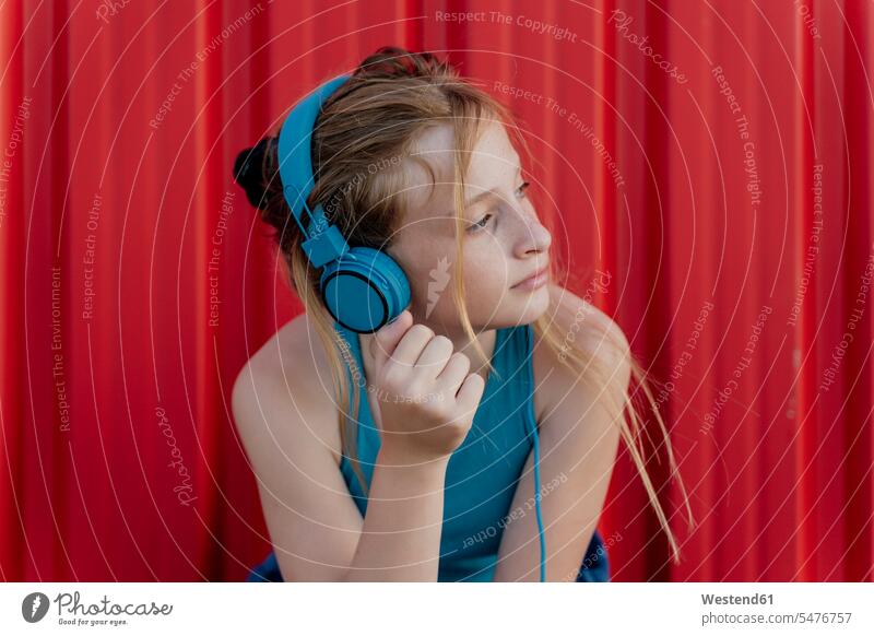 Mädchen mit Kopfhörern vor roter Wand T-Shirts Kopfhoerer entspannen relaxen hoeren geniessen Genuss zufrieden blaue blauer blaues rotes Muße Spass spassig
