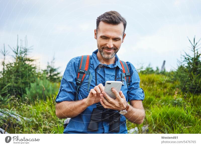 Lächelnder Mann überprüft sein Handy während einer Wanderung Männer männlich checken lächeln Wandertour Mobiltelefon Handies Handys Mobiltelefone wandern