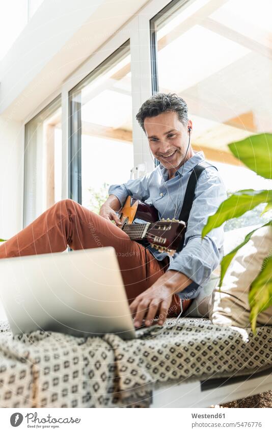 Reifer Mann übt auf der Gitarre, mit Laptop und Kopfhörern Instrument Instrumente Musikinstrumente Saiteninstrumente Gitarren Couch Couches Liege Sofas Rechner