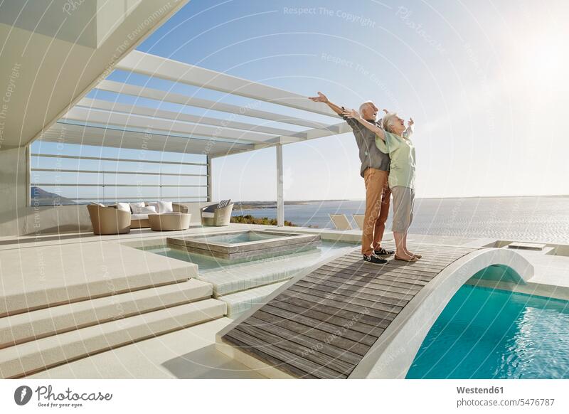 Sorgenfreies älteres Ehepaar steht auf einer Brücke über einem Swimmingpool in einem luxuriösen Strandhaus Touristen entspannen relaxen entspanntheit relaxt