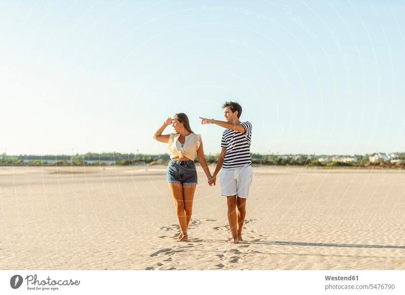 Junges Paar zu Fuß Hand in Hand am Strand Beach Straende Strände Beaches gehen gehend geht Pärchen Paare Partnerschaft Mensch Menschen Leute People Personen