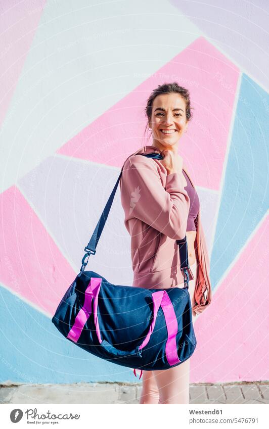 Sportliche Frau mit Sporttasche schaut in die Kamera Taschen rennen freuen Glück glücklich sein glücklichsein zufrieden pinkfarben rosa rosafarben Muße fit