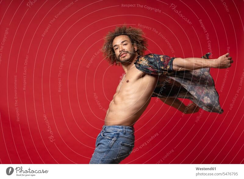 Junger Mann mit vollständig aufgeknöpftem Hemd tanzt vor rotem Hintergrund Farbaufnahme Farbe Farbfoto Farbphoto Spanien Millennials junge Erwachsene erwachsen