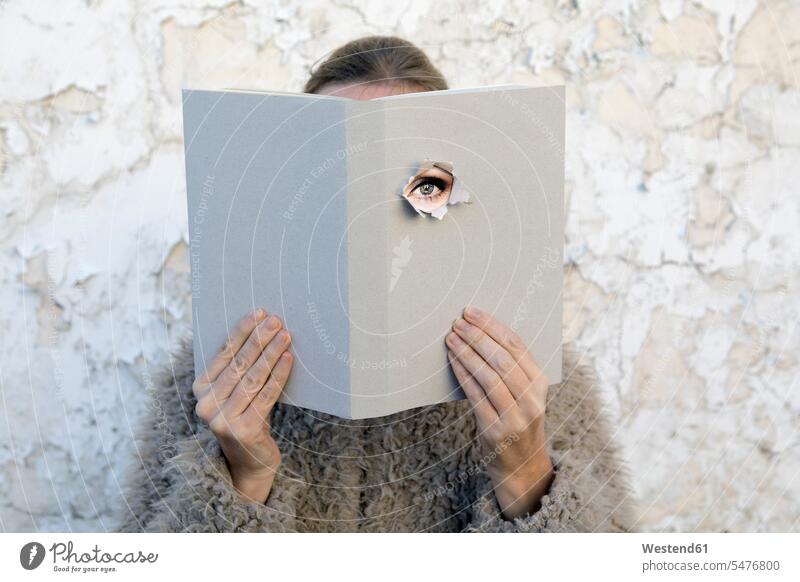 Frau bedeckt Gesicht mit Buch, liest Gedichte, Auge schaut durch den Einband Poesie lesen Mauer Gesicht verdeckt geheimnisvoll Wand Mensch Erwachsener spannend