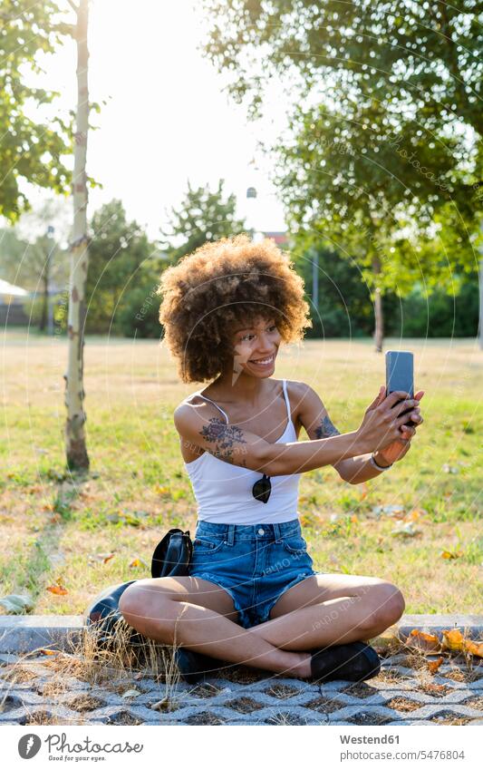 Porträt einer tätowierten jungen Frau, die im Sommer ein Selfie mit ihrem Smartphone macht Leute Menschen People Person Personen gemischtrassig 1 Ein ein Mensch
