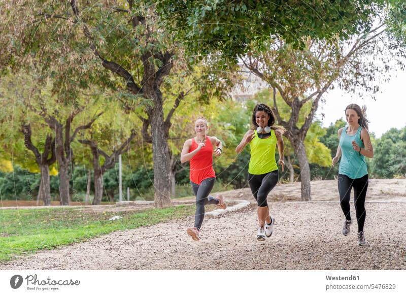 Drei sportliche junge Frauen laufen in einem Park Freunde Kameradschaft Freundin Kopfhoerer rennen Jahreszeiten sommerlich Sommerzeit freuen Frohsinn