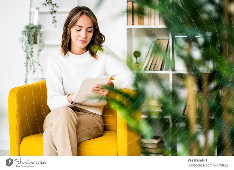 Geschäftsfrau benutzt digitales Tablet, während sie im Büro auf dem Sofa sitzt Farbaufnahme Farbe Farbfoto Farbphoto Innenaufnahme Innenaufnahmen innen drinnen