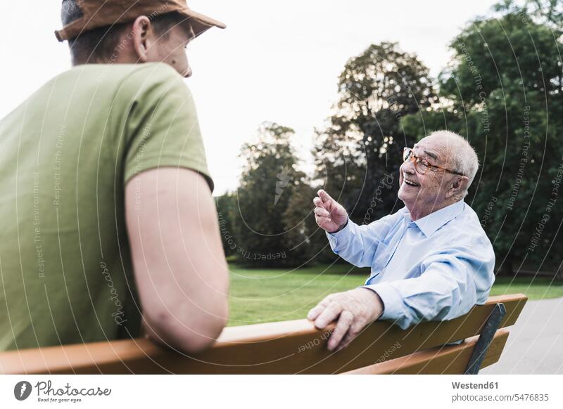 Glücklicher älterer Mann entspannt sich zusammen mit seinem Enkel auf einer Parkbank Generation sitzend sitzt reden entspannen relaxen entspanntheit relaxt