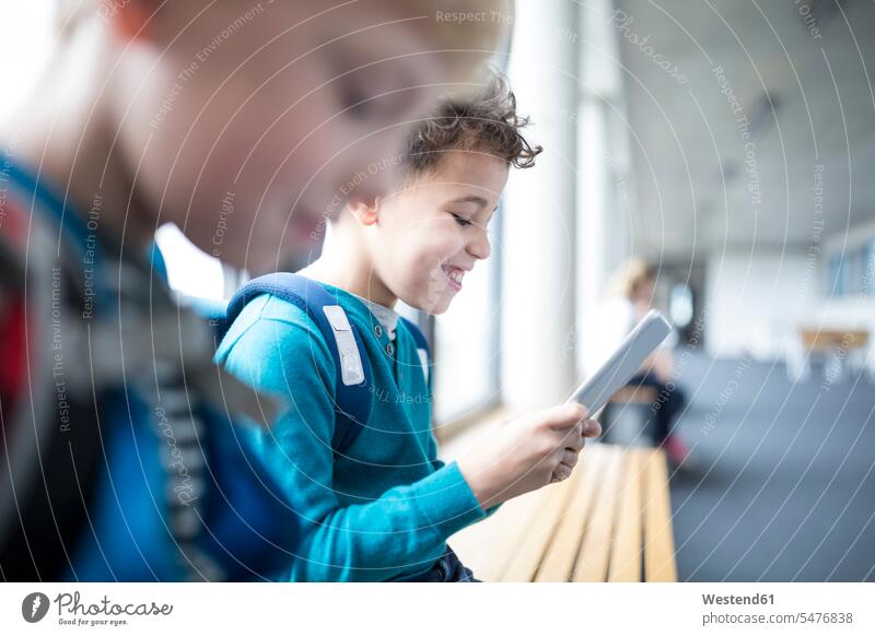 Lächelnde Schüler mit Tablette auf dem Schulkorridor Korridor glücklich Schule lächeln Schulkind Bildung Glück Computer Schulpause WLan Flur E-Learning sitzen