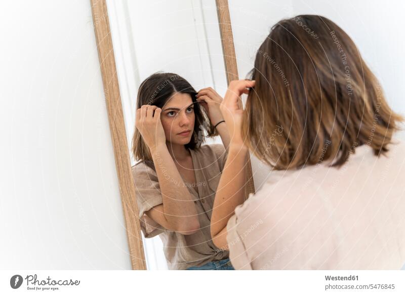Brünette junge Frau beim Blick in den Spiegel daheim zu Hause kontrollieren alltäglich Schoenheit Schönheit Attraktivität gut aussehend gutaussehend hübsch