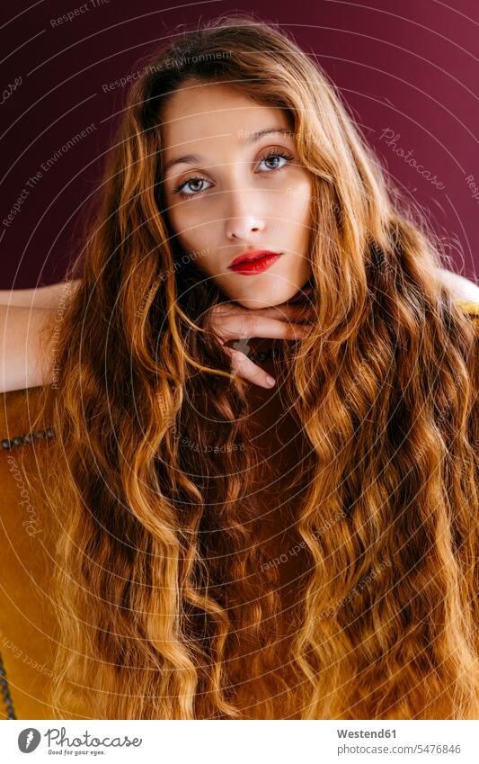 Porträt einer jungen Frau mit langem, braunem, gewelltem Haar, die auf einem Stuhl vor einem farbigen Hintergrund lehnt Farbaufnahme Farbe Farbfoto Farbphoto
