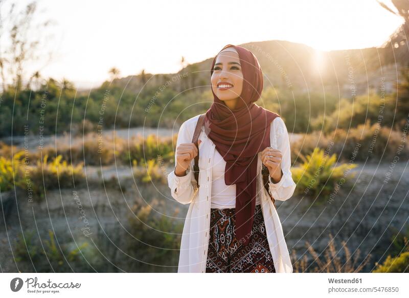 Lächelnde junge Touristin trägt Hijab in Wüstenlandschaft und schaut sich um Rucksäcke Kopftücher verreisen Wanderung freuen Glück glücklich sein glücklichsein