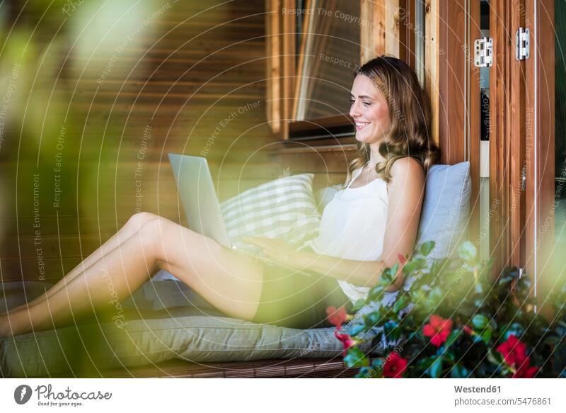 Lächelnde Frau auf Balkon mit Laptop entspannt entspanntheit relaxt Balkone weiblich Frauen lächeln Notebook Laptops Notebooks Entspannung relaxen entspannen