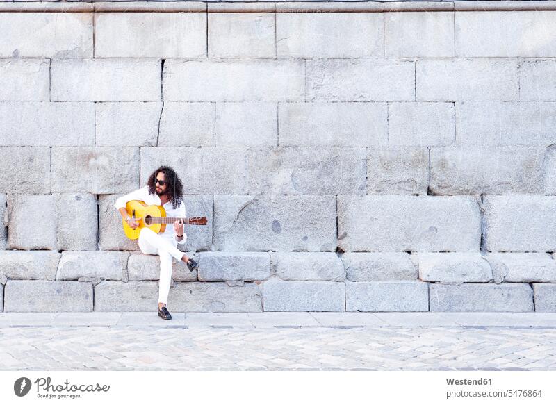 Gitarrist spielt Gitarre, während er an einer Betonwand sitzt Farbaufnahme Farbe Farbfoto Farbphoto Außenaufnahme außen draußen im Freien Tag Tageslichtaufnahme