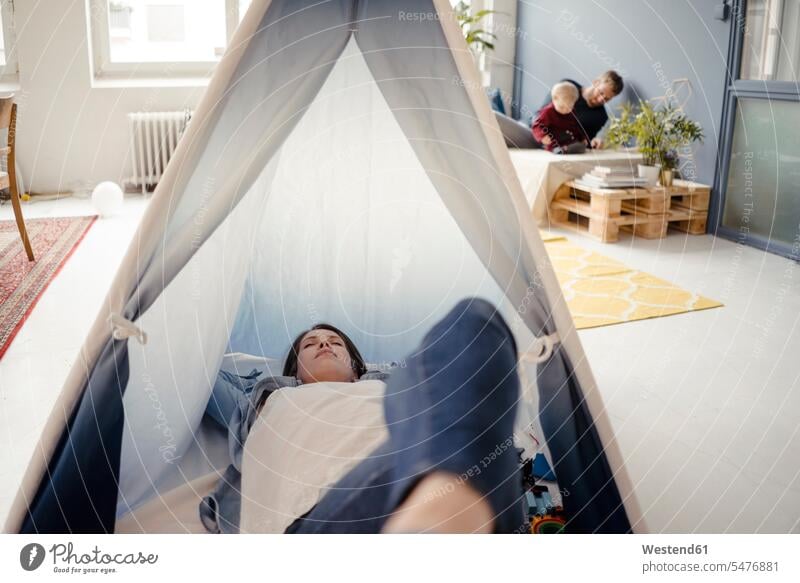 Frau ruht sich im Zelt aus, während der Vater im Hintergrund mit ihrem Sohn spielt weiblich Frauen Zelte müde abgespannt schlafen schlafend ausruhen Rast
