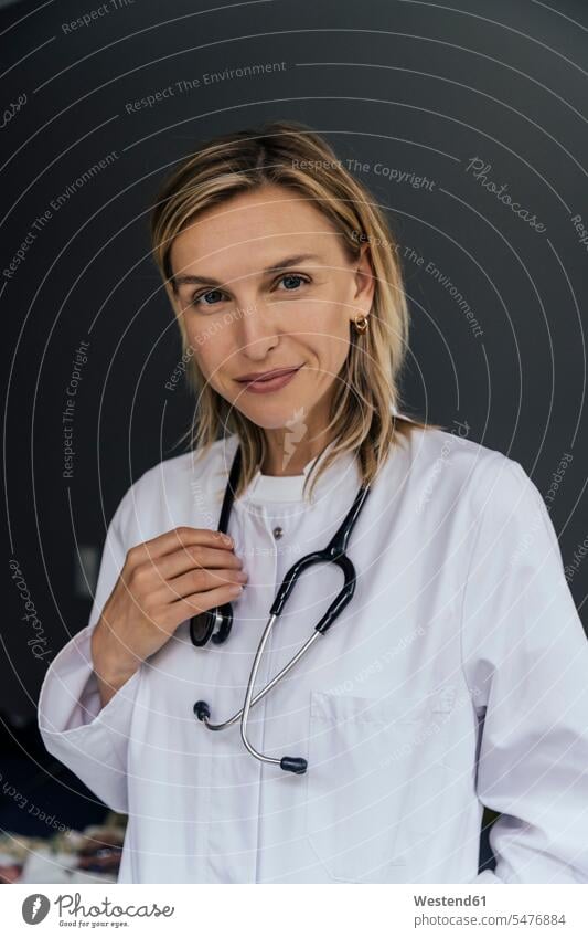 Porträt eines Arztes mit Stethoskop vor grauem Hintergrund Job Berufe Berufstätigkeit Beschäftigung Jobs Berufsbekleidung Gesundheit Gesundheitswesen