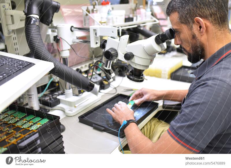 Mann, der ein Mikroskop zur Qualitätskontrolle bei der Herstellung von Leiterplatten für die Elektronikindustrie benutzt Qualitätsprüfung Fabrik Fabriken