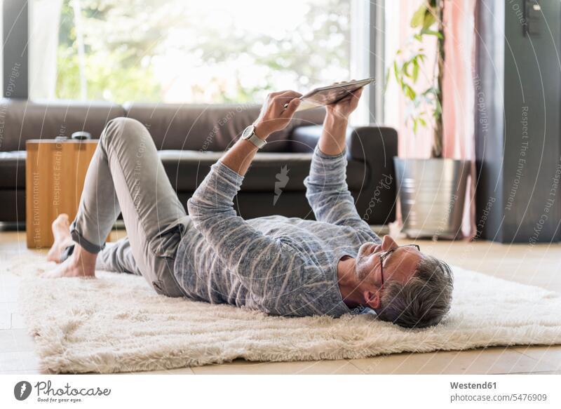 Reifer Mann, der zu Hause mit einer Tablette auf dem Teppich liegt Zuhause daheim Teppiche liegen liegend Männer männlich Tablet Computer Tablet-PC Tablet PC