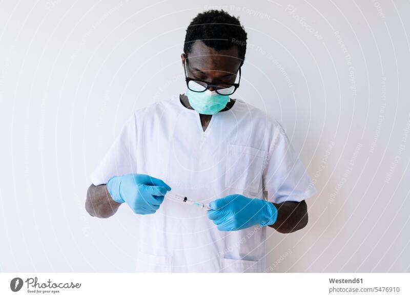 Afro-Arzt hält Spritze und Ampulle, während er vor weissem Hintergrund steht Farbaufnahme Farbe Farbfoto Farbphoto Spanien weißer Hintergrund