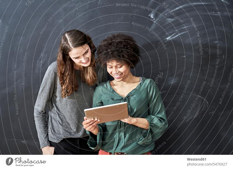 Zwei lächelnde junge Frauen teilen sich eine Tablette vor der Tafel Schultafeln Teilen Sharing Tablet Computer Tablet-PC Tablet PC iPad Tablet-Computer weiblich