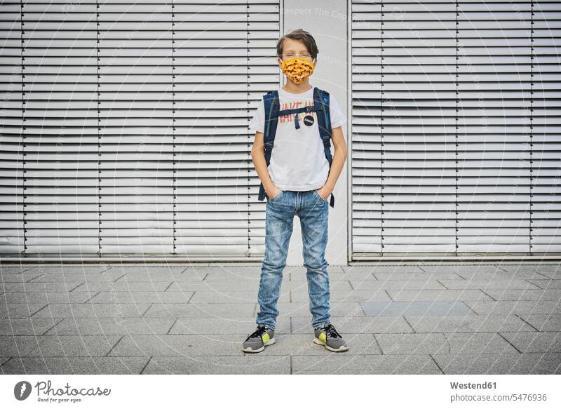Junge mit Schultasche mit Maske vor dem Gebäude stehend Leute Menschen People Person Personen Europäisch Kaukasier kaukasisch 1 Ein ein Mensch eine