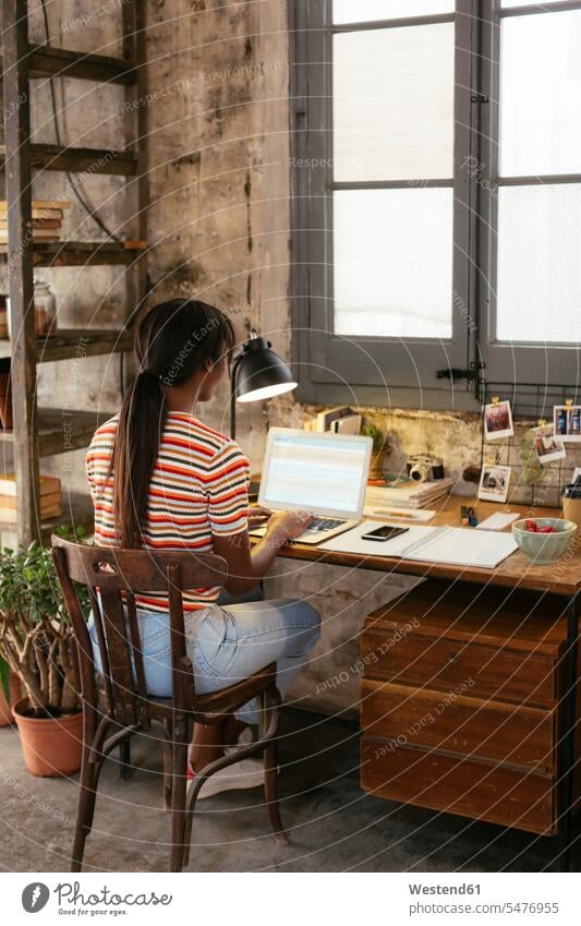 Rückenansicht einer jungen Frau, die in einem Loft am Schreibtisch sitzt und am Laptop arbeitet Notebook Laptops Notebooks sitzen sitzend Lofts weiblich Frauen