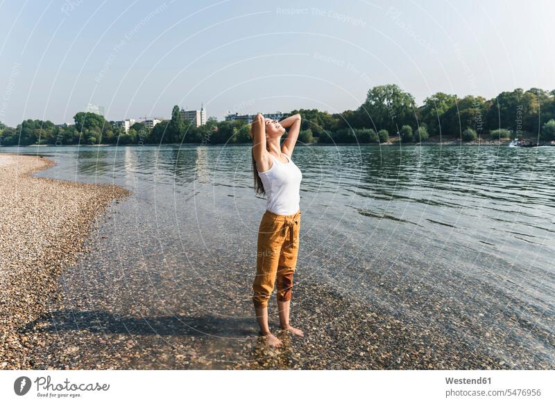 Glückliche junge Frau steht entspannt im Wasser eines Flusses entspanntheit relaxt Flussufer glücklich glücklich sein glücklichsein Fluesse Fluß Flüsse stehen