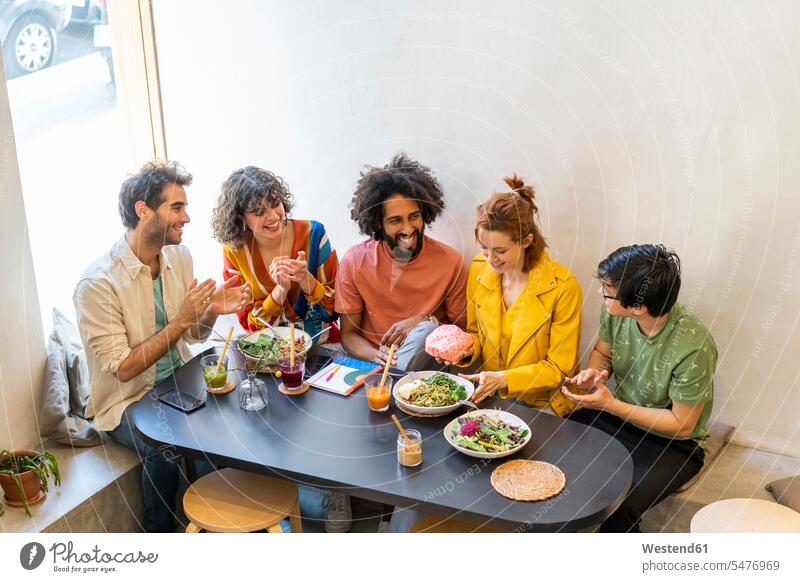 Gruppe von Freunden beim Mittagessen in einem Restaurant Gläser Trinkglas Trinkgläser Tische applaudieren Applaus Beifall sitzend sitzt freuen Frohsinn