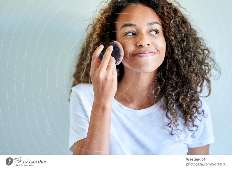 Lächelnde junge Frau Anwendung Gesichtspuder mit Make-up-Pinsel gegen weiße Wand Farbaufnahme Farbe Farbfoto Farbphoto Innenaufnahme Innenaufnahmen innen