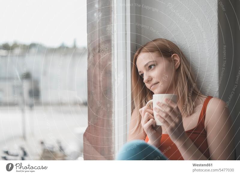 Porträt einer nachdenklichen jungen Frau mit einer Tasse Kaffee, die aus dem Fenster schaut Leute Menschen People Person Personen Alleinstehende Alleinstehender
