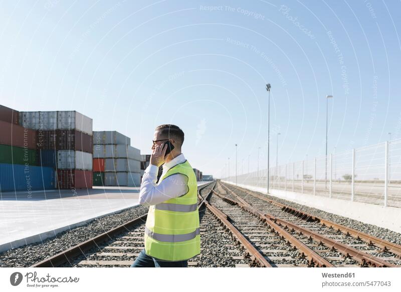 Mann auf Bahngleisen vor Frachtcontainern im Gespräch mit dem Handy Spanien Nachricht Mitteilung Botschaft Export exportieren Import Warenumschlag